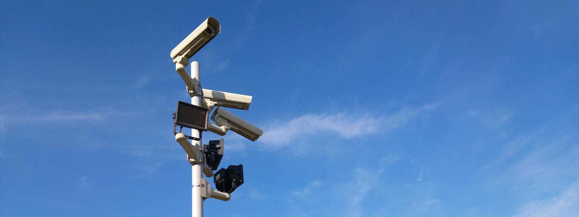 A multitude of CCTV cameras on a pole with spotlights.